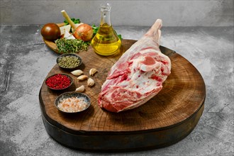 Raw whole lamb leg chump on with ingredients on wooden stump