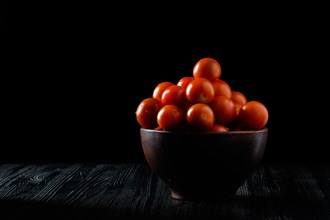 Low key photo of fresh tomato cherry in clay bowl