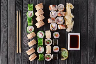 Large set of rolls with garnish and hashi on wooden plate