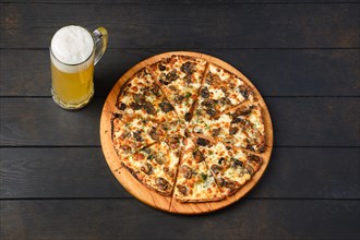 Top view of thin dough pizza with mushroom and a glass of lager beer on a table