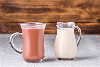Chocolate milk and soy milk in glass on white table over dark wooden background