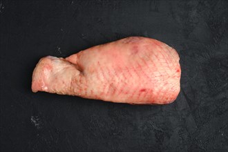 Raw half of turkey breast with bone and skin on dark background