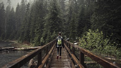 Female hiker walking wooden bridge leading toward forest