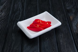 Pieces of chilli in plate on dark wooden background