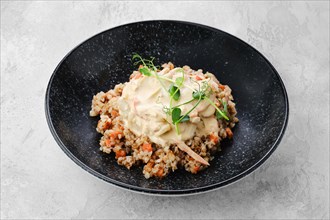 Buckwheat porridge with slices of fried carrot and creamy flour sauce on a plate