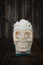 Halloween cocktail in goblet skull on wooden shelf. White monk drink in glass cup in the shape of skull