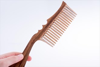 Hand holding a wooden hair comb on a white background