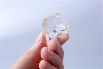 Hand holding a transparent diamond on a white background