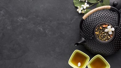 Dried tea herb ingredient with black teapot slate stone background