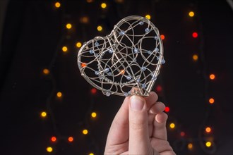 Heart shaped metal cage in hand on bokeh light background