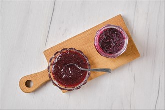 Overhead view of homemade blueberry jam in a jar and saucer on wooden serving board