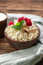 Fresh cottage cheese with raspberries and wooden spoon in clayware on wooden table