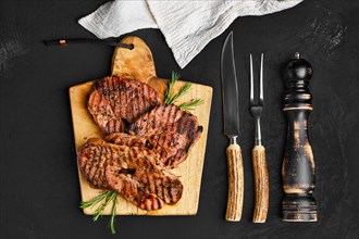 Overhead view of juicy steak on wooden cutting board over black background