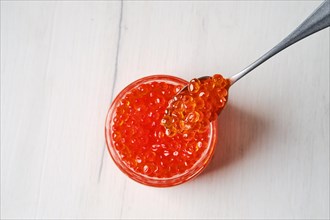Overhead view of open jar with red caviar and a spoon above it