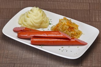 Plate with fried small sausage with mashed potato and cabbage on wooden table