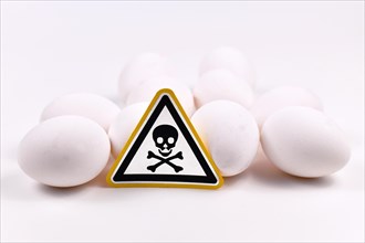 Concept for unhealthy or toxic substances in food like antibiotic residues or salmonella bacteria with skull warning sign on raw eggs on white background