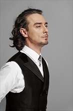Dramatic man in white shirt and black vest with long curly hair standing in profile