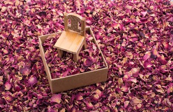 Toy chair on a box filled with dry rose petals