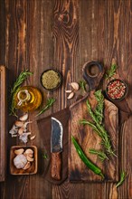 Overhead view of wooden cutting board with fresh rosemary and spices for piquant sauce or marinade on wooden kitchen table