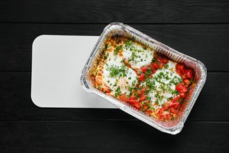 Overhead view of eggs fried with ham and tomato in take away foil package