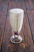 Glass of black currant milkshake on wooden table