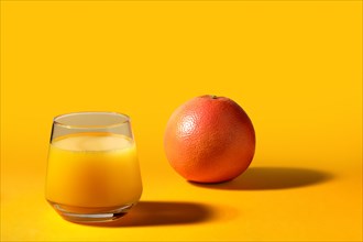 Glass with orange juice and whole fresh orange on bright background with long shadows