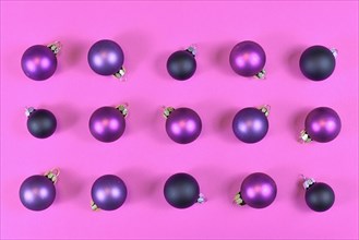 Purple Christmas tree bauble ornaments symmetrical arranged on pink background