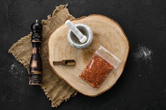 Wooden cross section with chili flakes in plastic package and stone mortar and mill