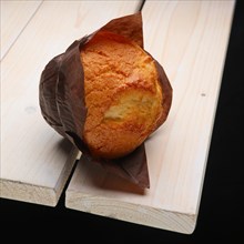 Fresh muffin in paper wrapper on the corner of wooden table
