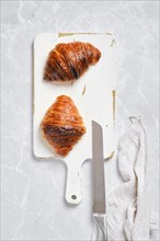 Top view of crispy croissant on white serving board on marble background