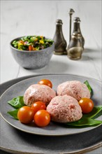 Semifinished frozen veal meatballs on a plate with basil and tomato