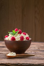 Wooden spoon with sour cream near clay plate with fresh cottage cheese with raspberries and mint