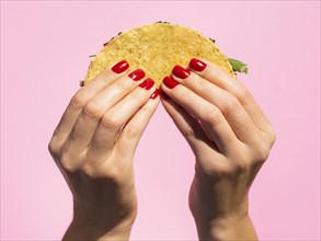 Close up hands holding taco with pink background