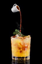 Pouring hot espresso in glass with tonic and orange syrup and thyme on black background