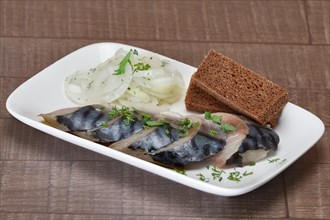 Plate with pickled herring and onion rings with slices of brown bread