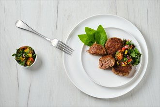 Top view of fried veal meatballs on a plate with basil and tomato