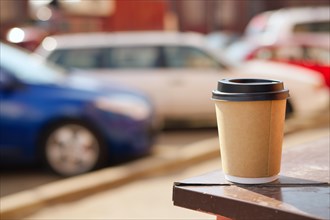 Cardboard cup of coffee on window sill. Blurred car parking on background