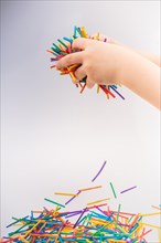 Hand letting coloured wooden sticks fall on white background