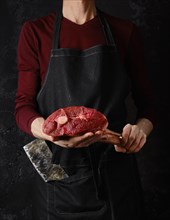 Butcher holds raw lamb leg in hands over dark background