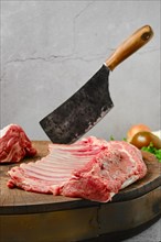Raw whole rack of lamb on wooden slab with butcher cleaver
