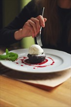 Shallow depth of foeld photo of brownie cake with ice-cream. Hand of girl with fork