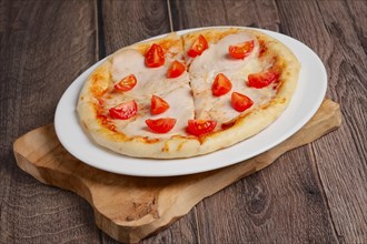 Pizza with ham and tomato on wooden plate