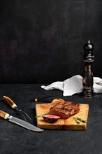 Juicy steak on wooden cutting board over black background