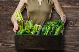 Unrecognizable wooman holds in hands wooden box with various fresh green vegetables
