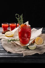 Selective focus composition with vodka and tomato juice cocktail served with citrus and rosemary on rough paper and fabric over the wooden table
