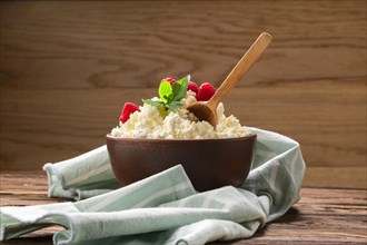 Fresh cottage cheese with raspberries and wooden spoon in clayware on wooden table