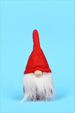 Cute Christmas gnome ornament with white beard and red hat on blue background