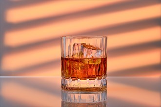 Whiskey with ice in facetted rocks glass over striped background