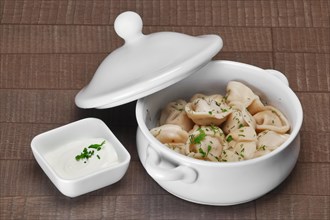 Bowl with hot boiled meat dumplings and sour cream on wooden table