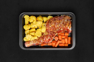 Overhead view of marinated lamb shoulder with potato and carrot in oven-tray